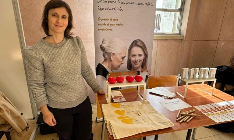 voluntaria ao lado de uma mesa com pecas de comunicacao da associacao e roll up por tras