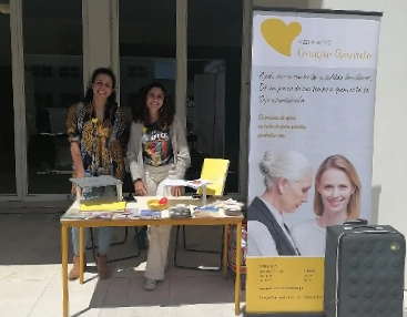 duas voluntarias num mesa com peças de comunicacao da associacao e roll up atras
