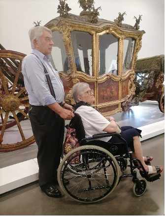 imagem de senhor a empurrar uma senhora de cadeira de rodas no museu dos coches